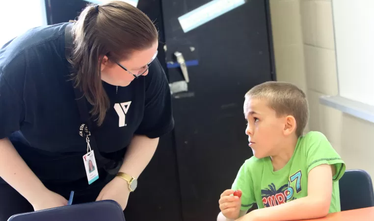 Educator bent over speaking with seated child