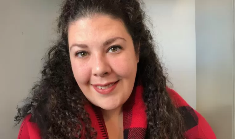 Jacqueline is wearing a red and black sweater and smiling at the camera.