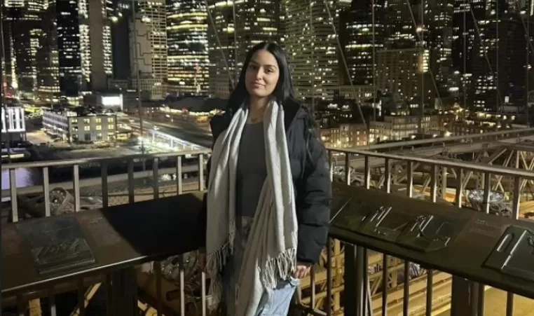 Young woman poses against the backdrop of a downtown city with skyscrapers at night.