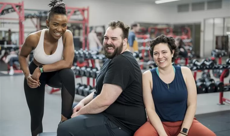 Three individuals sitting around at a gym smiling