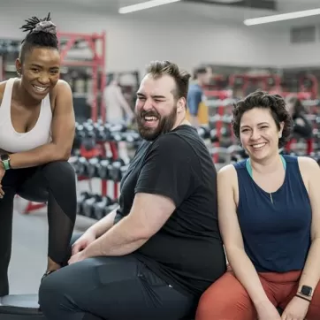 Three individuals sitting around at a gym smiling