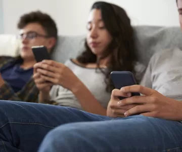 Three teenagers are sitting on the couch looking at their phones - the image is out of focus.