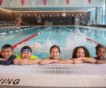 Five children in pool kicking feet and smiling